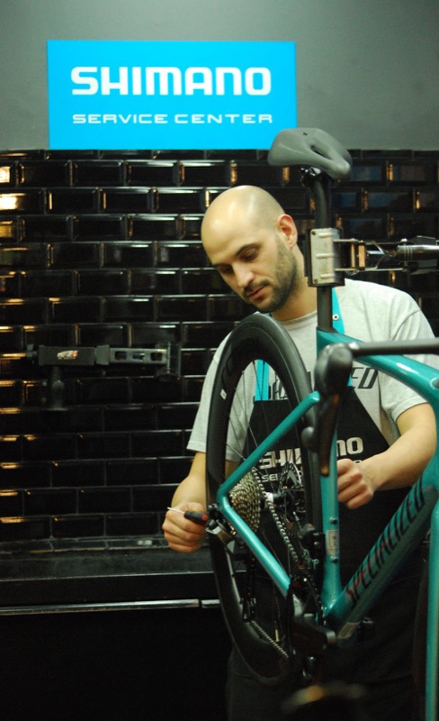 Un mecánico con una Specialized en el soporte, abajo del cartel de Shimano Service Center del taller